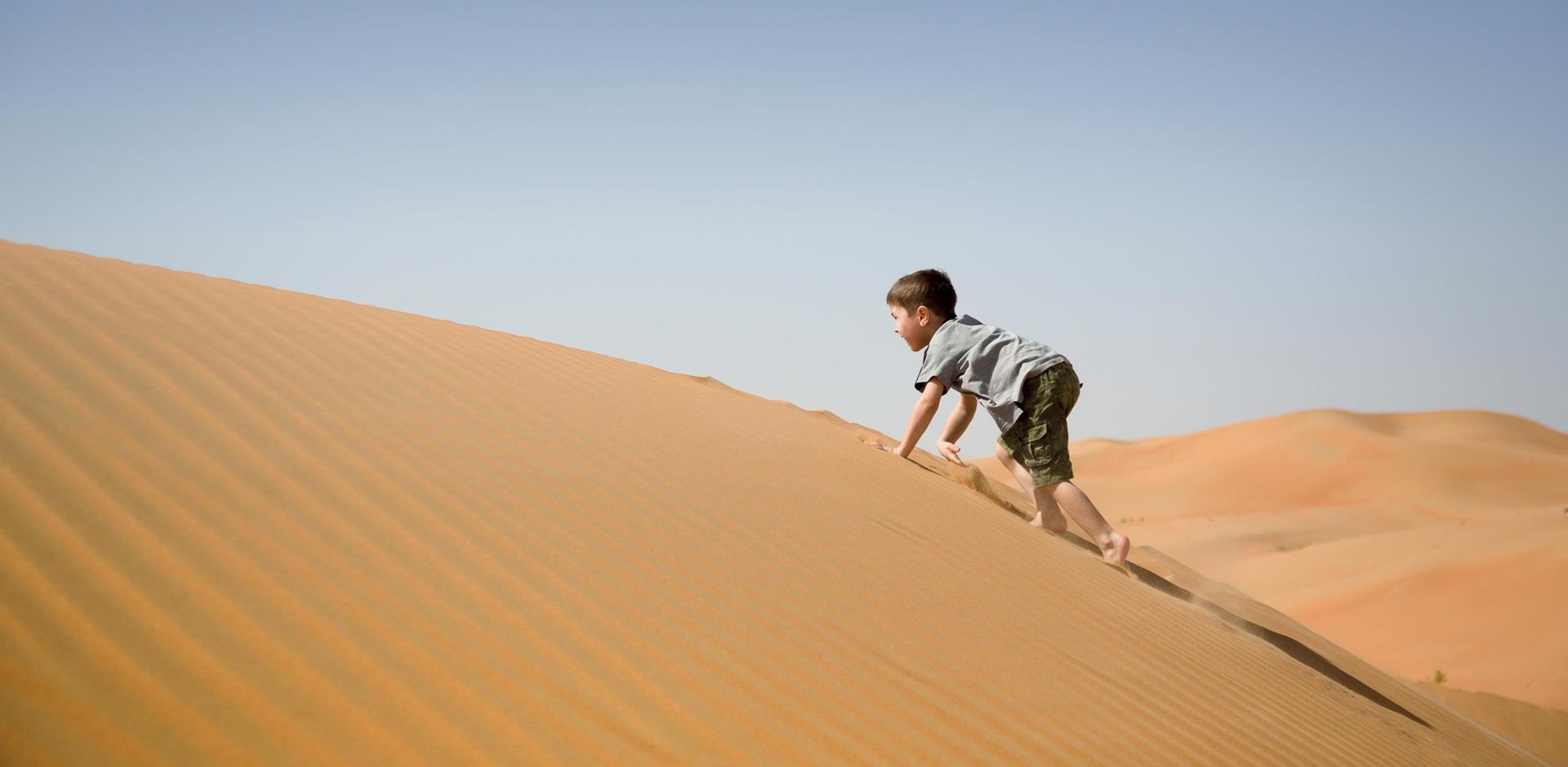 Boy climbing a sand dune in Oman